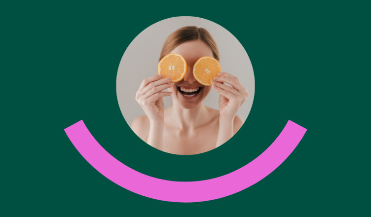 Eine lachende Frau hält zwei Orangenscheiben vor ihre Augen. Der Hintergrund ist dunkelgrün, unter dem Bild ist ein pinker, halbkreisförmiger Bogen wie ein stilisiertes Lächeln zu sehen.