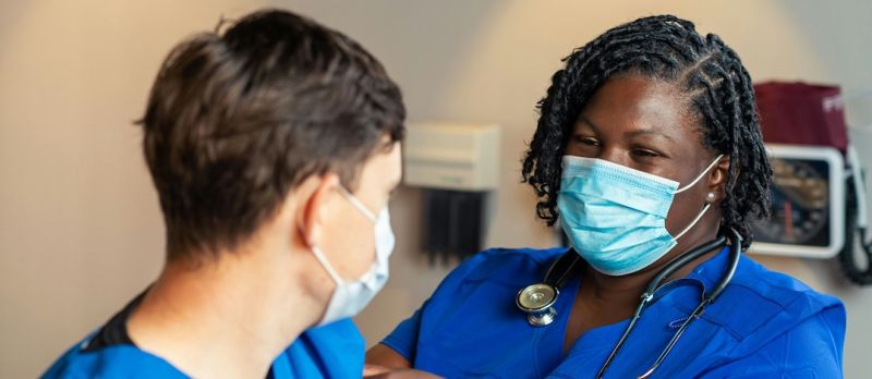 Nahaufnahme einer weiblichen Pflegekraft mit Mundschutz, die einen Patienten in einer Pflegeeinrichtung versorgt.