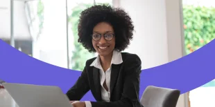 Lächelnde Frau sitzt an einem Tisch und arbeitet am Laptop.