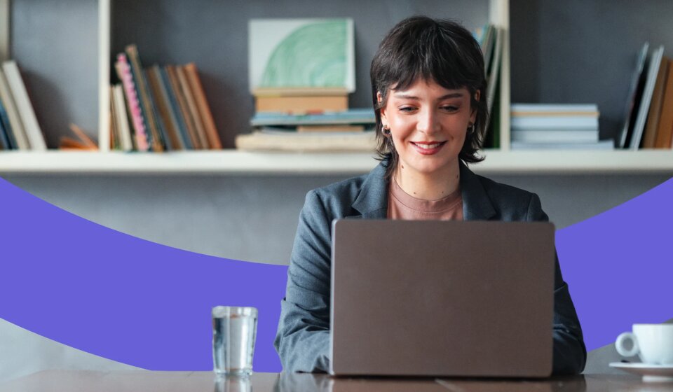 Frau sitzt an einem Tisch und arbeitet an ihrem Laptop.