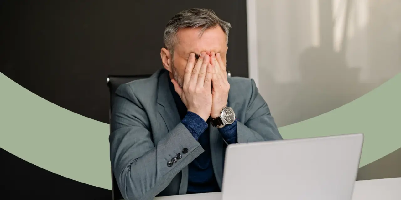 Mann sitzt am Schreibtisch und hält sich beide Hände vor das Gesicht.