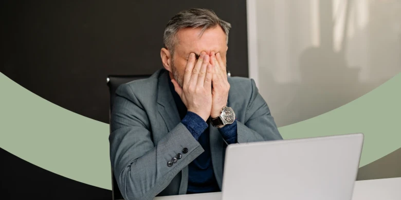Mann sitzt am Schreibtisch und hält sich beide Hände vor das Gesicht.