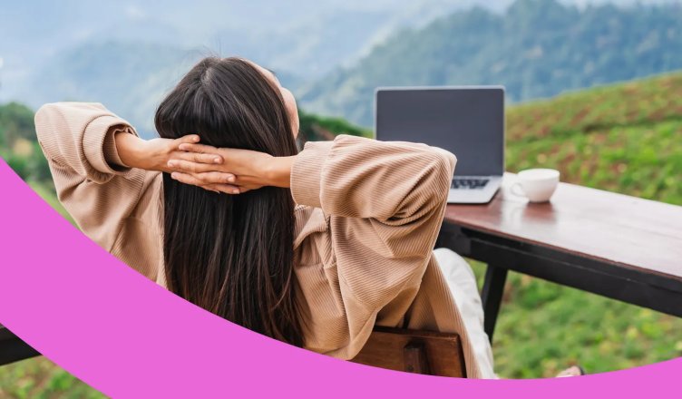 Frau sitzt entspannt mit Blick auf eine Berglandschaft vor ihrem Laptop.